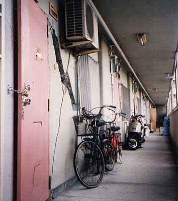 全壊判定の集合住宅の廊下。X字型にひびが入り内部が見え、ドアも閉まらない。/長田区 1995年2月